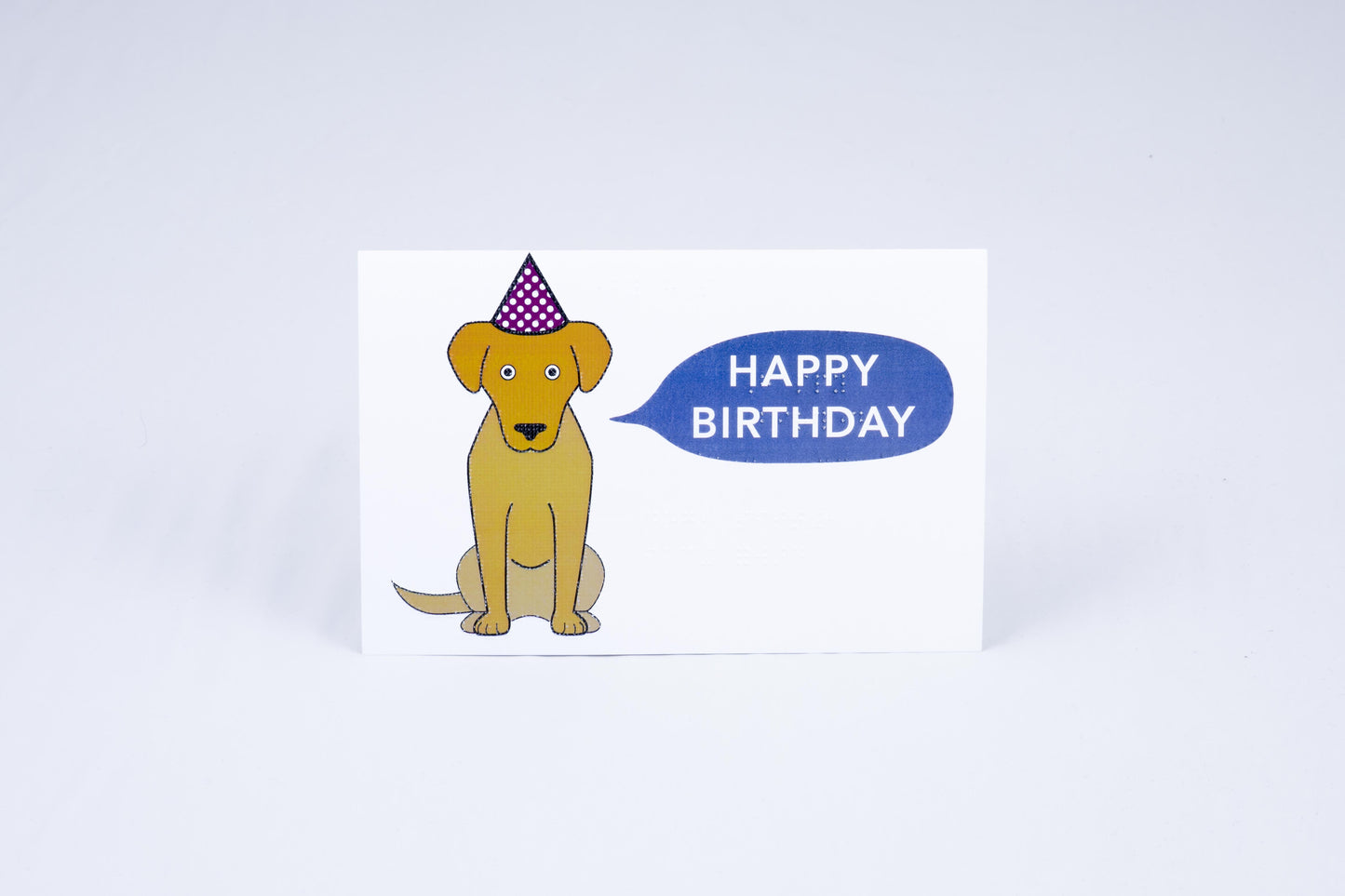 Jeep the golden labarador, staring directly at the reader wearing a birthday hat. Next to him is a speech bubble which reads "Happy Birthday" in print and Braille.